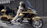 Rider performing a burnout on a gold Honda Gold Wing touring motorcycle with helmeted rider in white gear