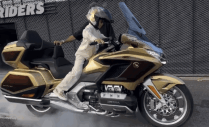 Rider performing a burnout on a gold Honda Gold Wing touring motorcycle with helmeted rider in white gear