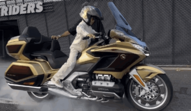 Rider performing a burnout on a gold Honda Gold Wing touring motorcycle with helmeted rider in white gear