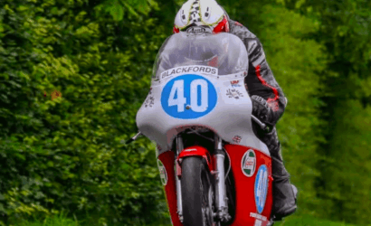 Rider on a vintage red racing motorcycle with number 40, wearing a white helmet, on a green leafy track.