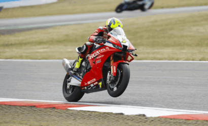 Rider on a red Honda sport bike taking a high-speed corner on a race track, helmet bright yellow.