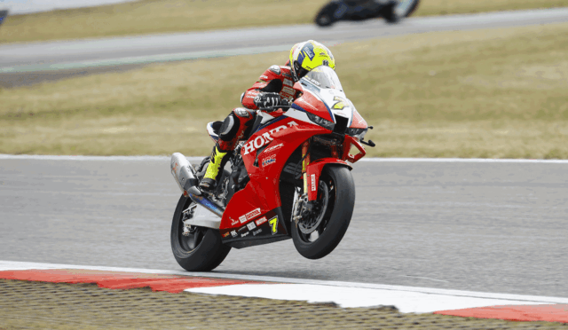 Rider on a red Honda sport bike taking a high-speed corner on a race track, helmet bright yellow.