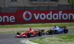 Red Formula 1 car leading a blue Renault behind on a race track with a large Vodafone sign in the background