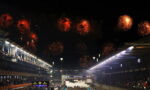 Nighttime motorsport finish with fireworks above a crowded grandstand and a lit finish line.