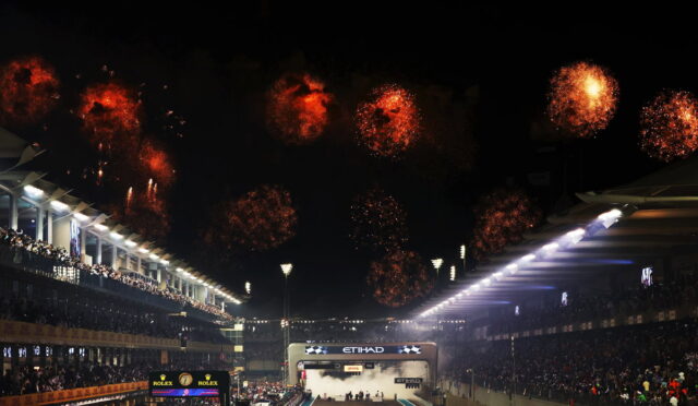 Nighttime motorsport finish with fireworks above a crowded grandstand and a lit finish line.