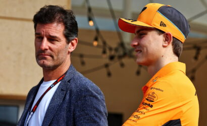 Man in a blue blazer and white shirt stands beside a young cyclist in an orange cap and jersey at an outdoor event.
