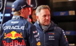 Two Red Bull Racing crew members in branded jackets chat in the pits, Oracle and Red Bull logos visible.