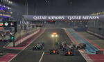 Nighttime Formula 1 race start: multiple cars line up on a illuminated track beneath a large Qatar Airways banner.",