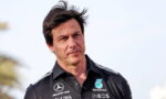 Man in a dark polo shirt with sponsor logos outdoors, looking thoughtful.