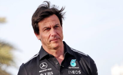 Man in a dark polo shirt with sponsor logos outdoors, looking thoughtful.