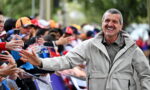 Smiling man in a light jacket greets a cheering crowd, extending a hand for a high-five along a barrier on a street event clarifying moment of interaction with fans.