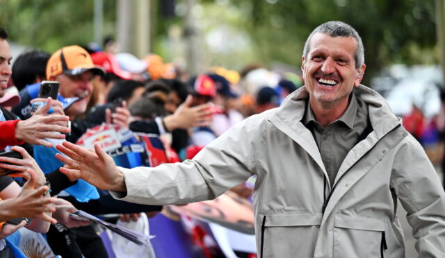Smiling man in a light jacket greets a cheering crowd, extending a hand for a high-five along a barrier on a street event clarifying moment of interaction with fans.