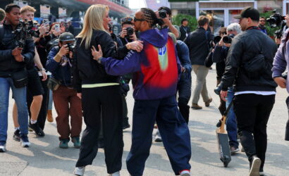Two people dancing arm-in-arm among a crowd of photographers at an outdoor event.