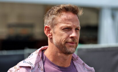 Portrait of a man with short light brown hair and graying beard, looking to the right, wearing a pink embroidered jacket over a purple shirt outdoors.