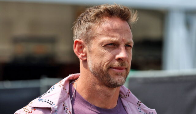 Portrait of a man with short light brown hair and graying beard, looking to the right, wearing a pink embroidered jacket over a purple shirt outdoors.