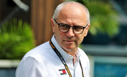 Portrait of a middle-aged man with black glasses wearing a white shirt and a lanyard, outdoors.