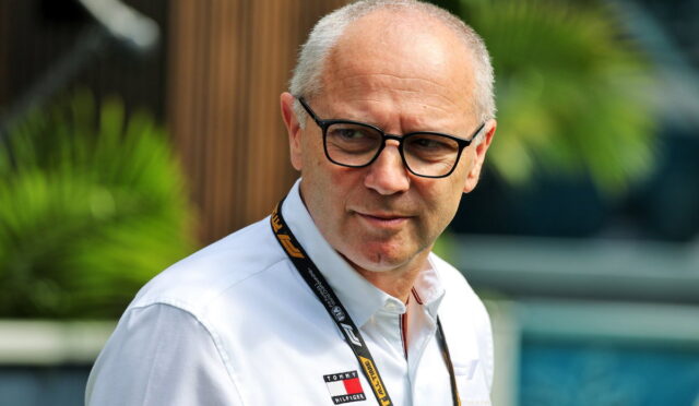 Portrait of a middle-aged man with black glasses wearing a white shirt and a lanyard, outdoors.