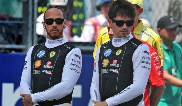 Two Formula 1 drivers in black-and-white Ferrari racing suits wearing sunglasses, standing with arms crossed at a track event, logos visible on suits (Shell, HP).