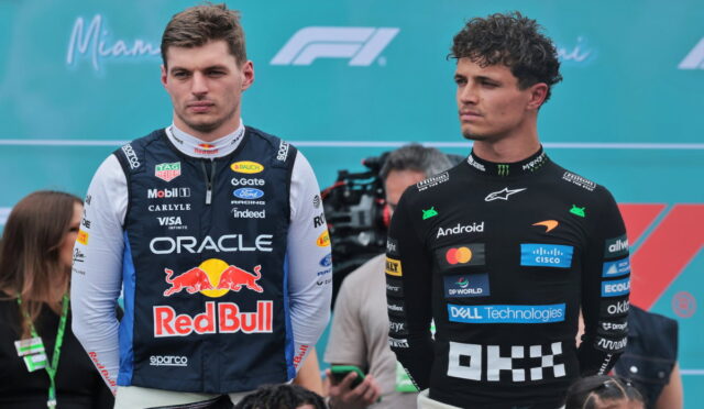 Two Formula 1 drivers stand side by side at a motorsport event, the left in an Oracle Red Bull racing suit and the right in a McLaren suit with sponsor logos, against a Miami F1 backdrop.