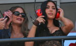 Two women in a VIP area wearing large headsets; one with sunglasses and a black lace top, the other adjusting her headset.