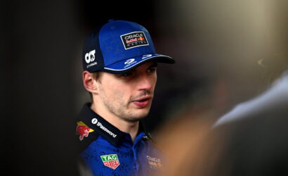 Male Formula 1 driver in blue cap with Oracle Red Bull Racing logo talking, wearing blue race suit with TAG Heuer and Mobil logos.