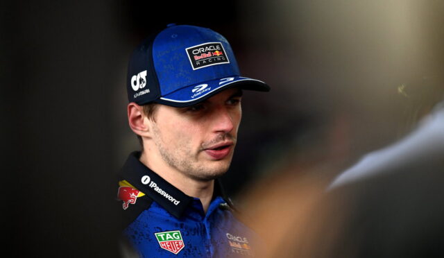 Male Formula 1 driver in blue cap with Oracle Red Bull Racing logo talking, wearing blue race suit with TAG Heuer and Mobil logos.