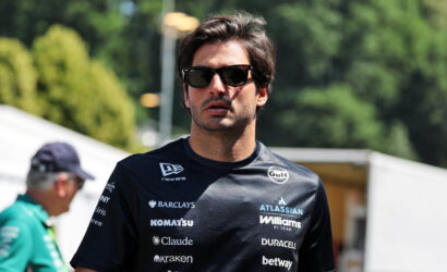 Man wearing a dark sponsor-logo shirt and sunglasses outdoors, looking to the side.