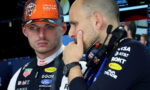 Two Red Bull Racing crew members in a garage, one wearing an orange cap, discussing strategy near equipment.