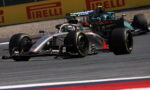 Silver Formula 1 car leading a race, 'Visit Qatar' on its side, speeding along a track with Pirelli boards in the background.