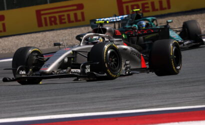 Silver Formula 1 car leading a race, 'Visit Qatar' on its side, speeding along a track with Pirelli boards in the background.