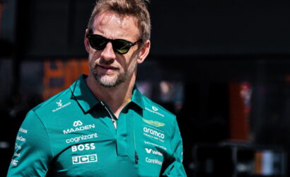 Man in a teal polo with sponsor logos and dark sunglasses, looking to the left outside.