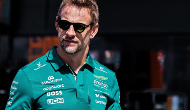 Man in a teal polo with sponsor logos and dark sunglasses, looking to the left outside.