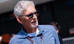 Older man with gray hair and beard, blue sunglasses, and a blue shirt, outdoors with a lanyard around his neck.