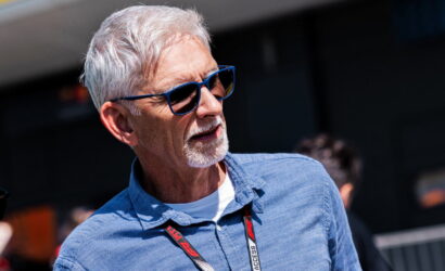 Older man with gray hair and beard, blue sunglasses, and a blue shirt, outdoors with a lanyard around his neck.
