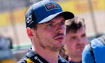 Close-up of a man wearing a blue Oracle Red Bull Racing cap, looking intently to the right at a race track.