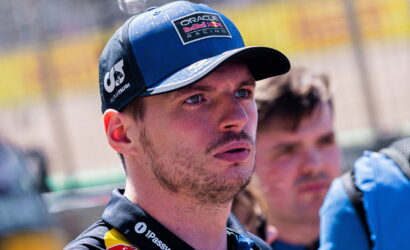 Close-up of a man wearing a blue Oracle Red Bull Racing cap, looking intently to the right at a race track.