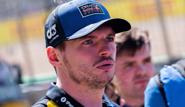 Close-up of a man wearing a blue Oracle Red Bull Racing cap, looking intently to the right at a race track.