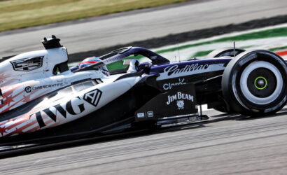 Formula 1 car speeding along a race track with sponsor logos on its white and black livery, driver in helmet visible