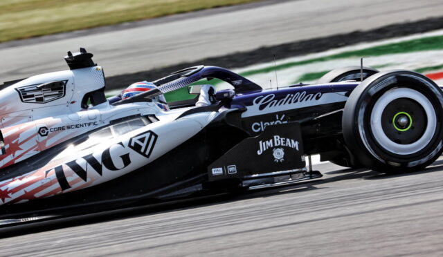 Formula 1 car speeding along a race track with sponsor logos on its white and black livery, driver in helmet visible