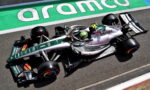 Formula 1 car in green and white livery speeding along a race track with Aramco branding visible on the track edge.