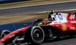 Red Formula 1-style race car speeds along a track, motion blurred with visible sponsor logos on its side wings and body.