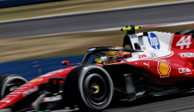Red Formula 1-style race car speeds along a track, motion blurred with visible sponsor logos on its side wings and body.