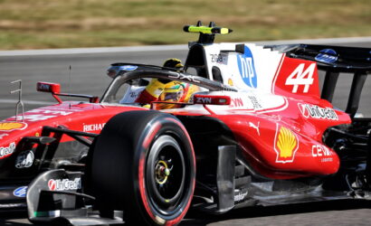 Red Formula 1 race car on a track with driver in yellow helmet, number 44 and Shell logo visible on the side