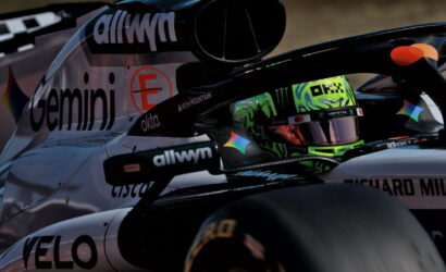 Close-up of a race car cockpit with a neon-green helmeted driver and sponsor logos on the body (informative)