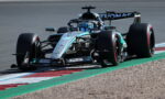 Mercedes-AMG Petronas F1 car speeding around a corner on a race track, visible blue helmeted driver and sponsor logos on the bodywork