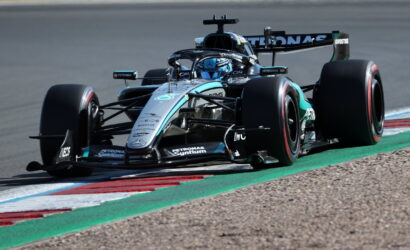 Mercedes-AMG Petronas F1 car speeding around a corner on a race track, visible blue helmeted driver and sponsor logos on the bodywork
