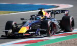 Red Bull Formula 1 car on a race track taking a tight turn, driver in helmet visible and sponsor logos on the car.