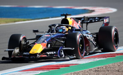 Red Bull Formula 1 car on a race track taking a tight turn, driver in helmet visible and sponsor logos on the car.