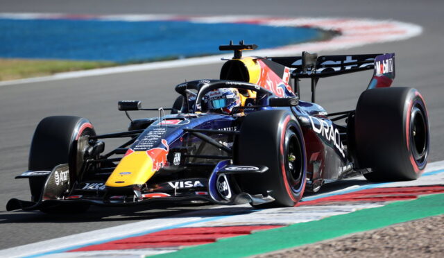 Red Bull Formula 1 car on a race track taking a tight turn, driver in helmet visible and sponsor logos on the car.