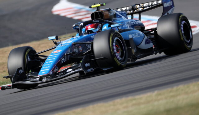 Blue Formula 1 race car taking a tight corner on a race track, with sponsor logos visible along the body and wing.